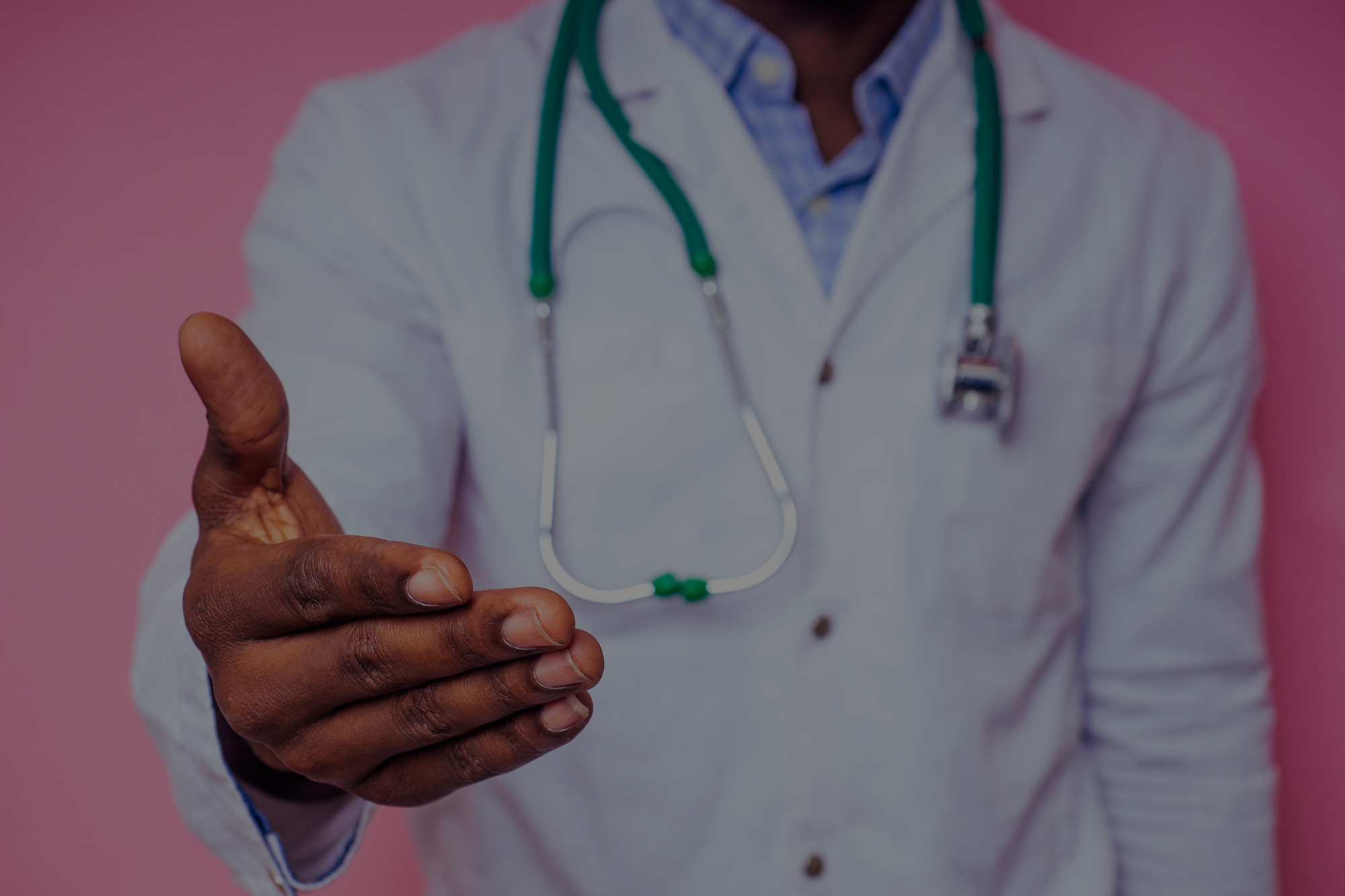 happy male african medical surgeon cardiologist doctor in a white coat holding out a hand for a handshake on a pink background in the studio.Welcome invitation gesture