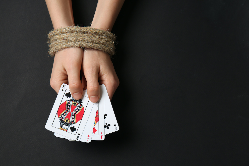 Woman with tied hands and playing cards on dark background. Concept of addiction